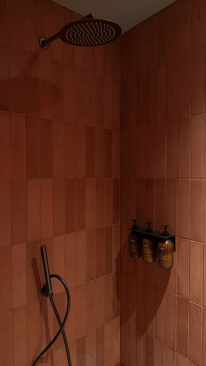 Ducha de baldosa terracota con tres frascos ámbar Wake by Etereo en un soporte negro